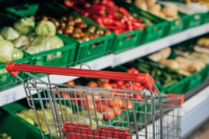 selective focus of empty shopping cart and fresh vegetables in supermarket